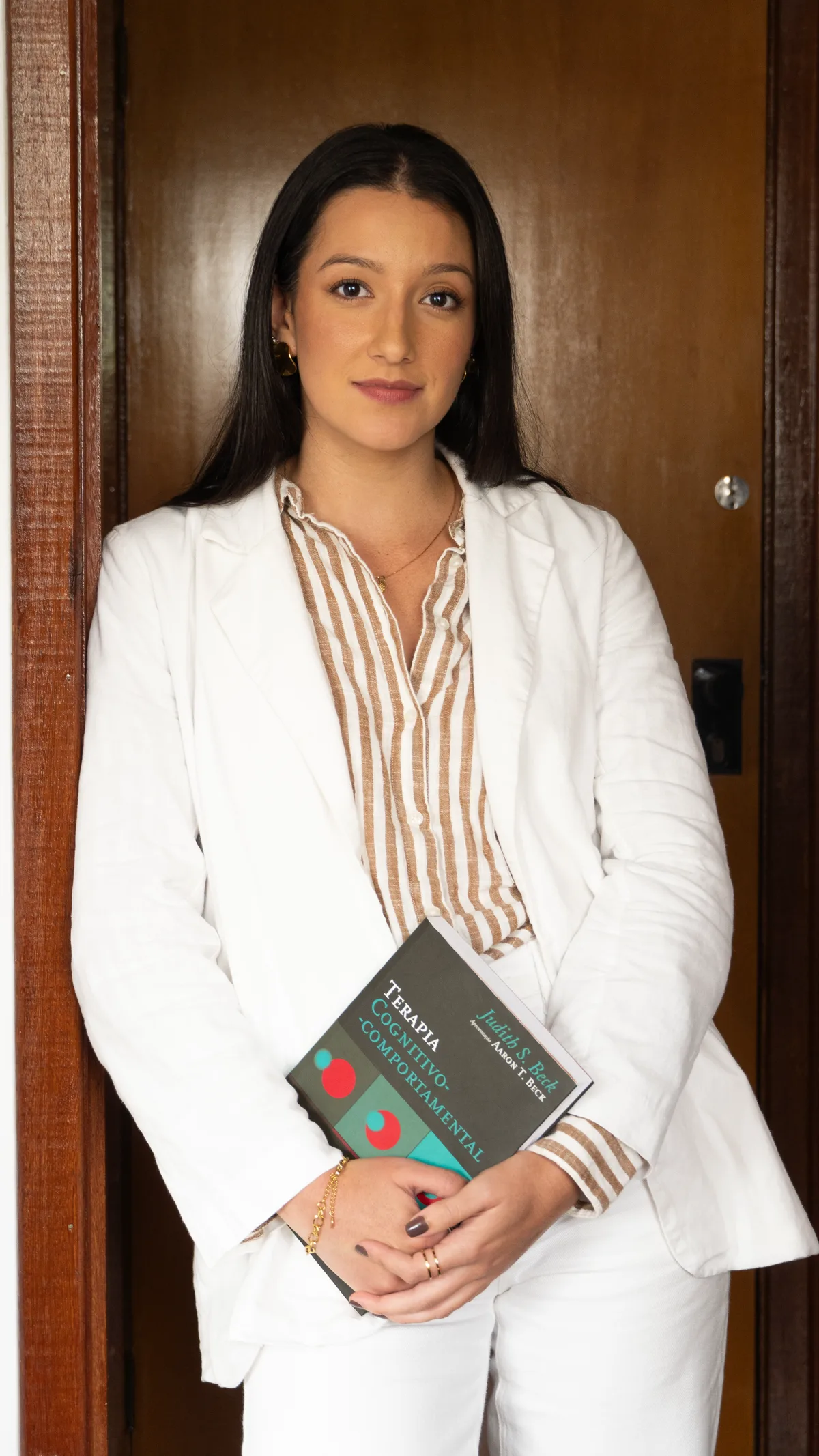 Retrato profissional de Taiane Oliveira segurando um livro de Terapia Cognitivo-Comportamental